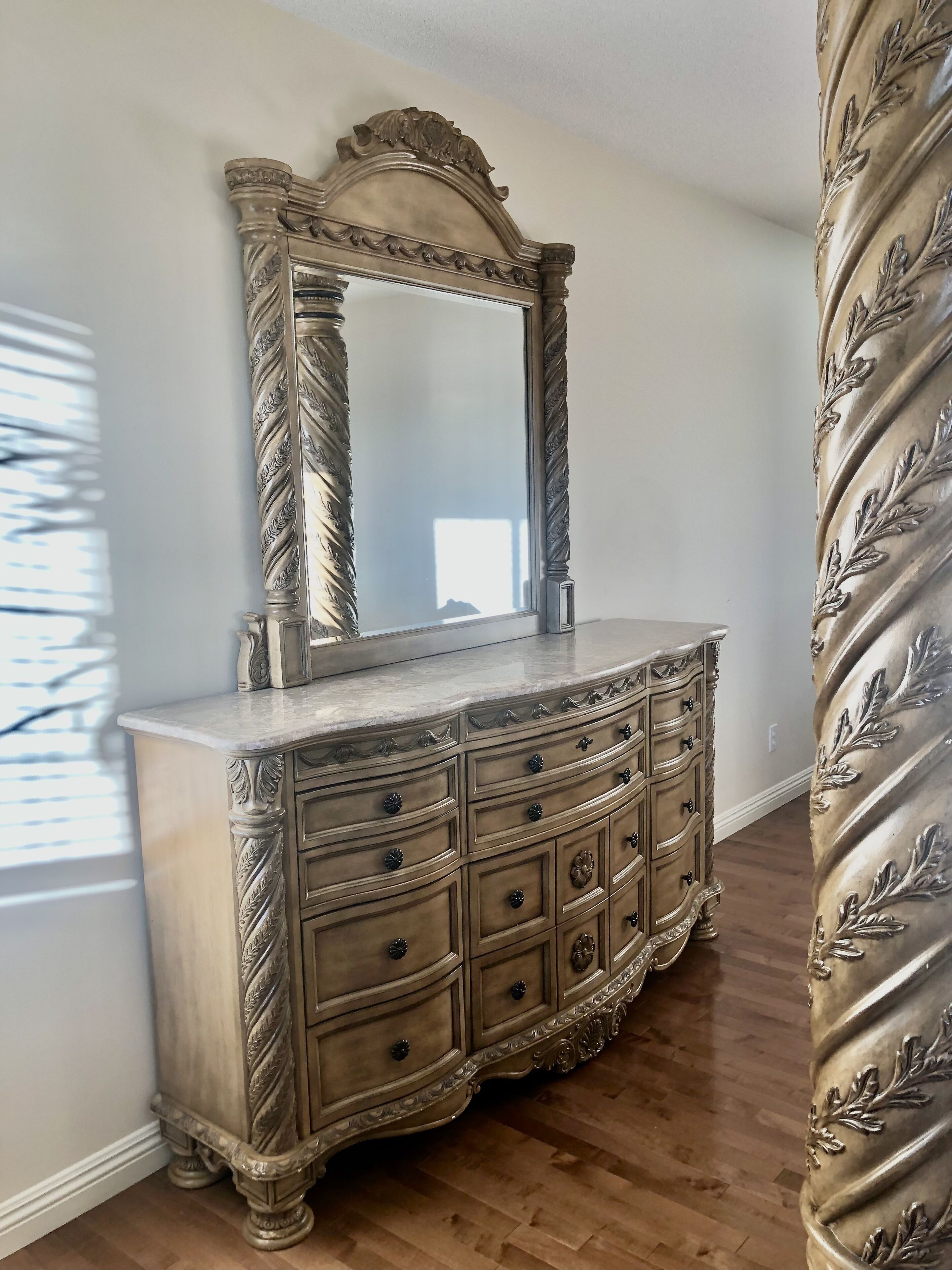 A large, ornate dresser with a mirror above it, positioned against a wall with a window.