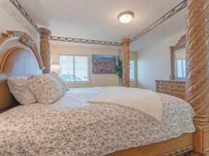 A bedroom with a four-poster bed, a wooden dresser, and a painting on the wall.