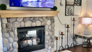Ein Wohnzimmer mit Kamin aus Stein, einem flachbildfernseher darüber und einem Glastisch mit einer dekorativen Schale.