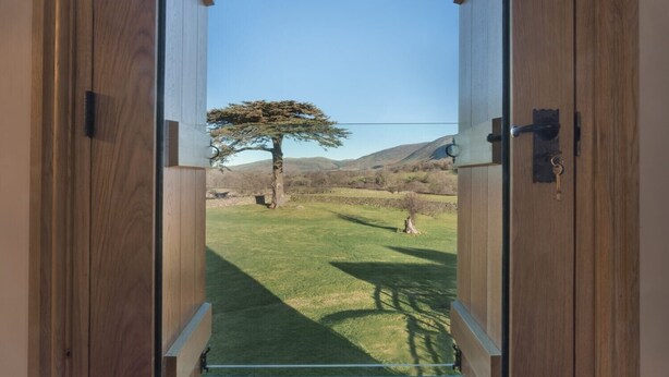 A wooden door leading to a grassy outdoor area with a tree and mountains in the background. - Cedar Nook (Cockermouth)