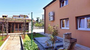 Una propiedad residencial con jardín, una pérgola, una fuente de agua de ladrillo y una casa de dos pisos con unidades de aire acondicionado.