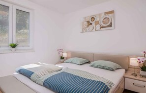 Une chambre à coucher comprenant un lit, deux tables de chevet, une fenêtre et une œuvre d’art accrochée au mur.