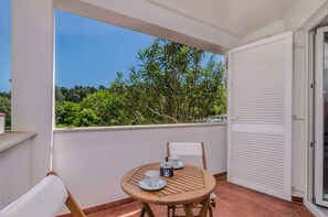 Un balcon avec une table et des chaises, une porte blanche et une vue sur les arbres.