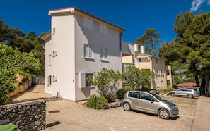 A two-story building with a stone wall, a paved driveway, and parked cars. - Holiday apartment on the ground floor (Dobrinj)