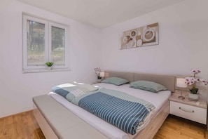 A bedroom with a bed, bedside tables, a window, and a wall art piece. - Holiday apartment on the ground floor (Dobrinj)