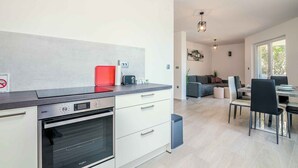 Eine moderne Küche mit Einbauofen, eine Essecke mit Tisch und Stühlen sowie ein Wohnbereich mit Sofa und Couchtisch.