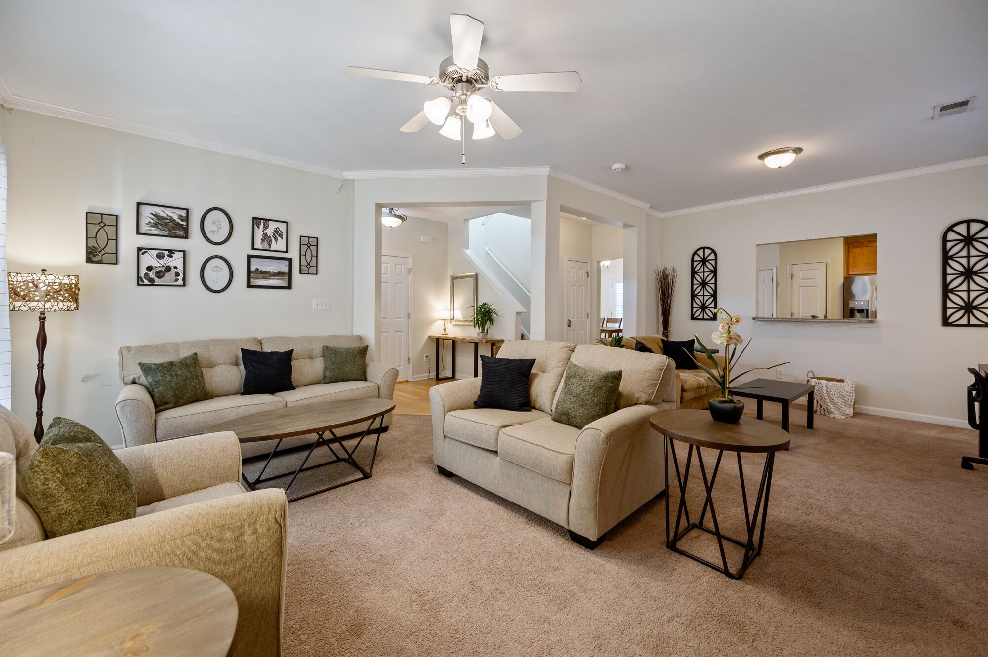 A spacious living room with a beige sofa set, a coffee table, and a ceiling fan.