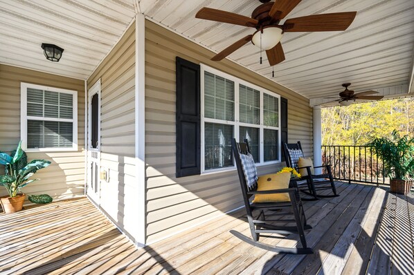 A covered porch with wooden flooring, a ceiling fan, and two rocking chairs with cushions.