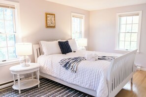 A bedroom with a white bed, two bedside lamps, a small round table, and a patterned rug.