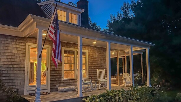 A two-story house with a covered porch, an American flag, and a well-lit entrance. - In-Ground Plunge Pool Dog Friendly! (Brewster)