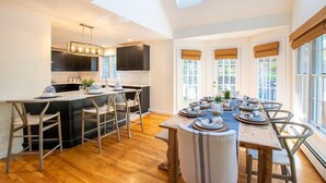 A modern kitchen with a central island, bar stools, and a dining area with a long table set for six. - In-Ground Plunge Pool Dog Friendly! (Brewster)