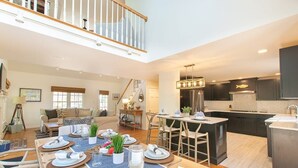 A spacious living area with a dining table set for a meal, a kitchen with dark cabinets, and a staircase leading to an upper level. - In-Ground Plunge Pool Dog Friendly! (Brewster)
