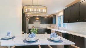 A modern kitchen with dark cabinetry, a central island with blue-patterned bowls, and a pendant light. - In-Ground Plunge Pool Dog Friendly! (Brewster)