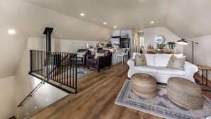 Un appartement-loft spacieux avec un plafond haut, un escalier doté d’une rampe noire, un canapé blanc, des fauteuils en cuir, un coin cuisine et une table à manger.
