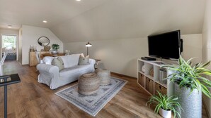 Un salon moderne avec un canapé blanc, des poufs, un téléviseur à écran plat et des plantes en pot.