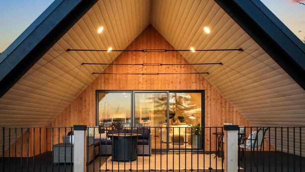 Une structure moderne en bois, dotée d’un toit incliné, de grandes portes vitrées et d’un patio clos agrémenté de mobilier d’extérieur.