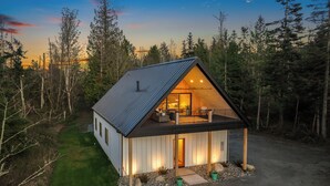 Une cabane avec un toit en pente, une véranda dotée de sièges d’extérieur et une vue sur la forêt environnante.