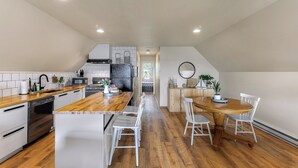 Une cuisine moderne avec un plan de travail en bois, des armoires blanches et un coin repas comprenant une table ronde et des chaises blanches.