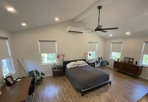 A bedroom with a bed, bedside tables, a desk, a ceiling fan, and large windows.