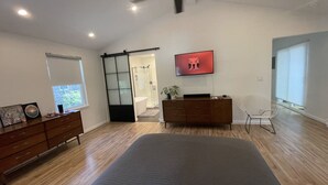 A modern bedroom with a large bed, a wooden dresser, a TV, and a sliding glass door leading to a bathroom. - 7 Miles to Masters Tournament - Less Traffic - Sleeps 8 (North Augusta)