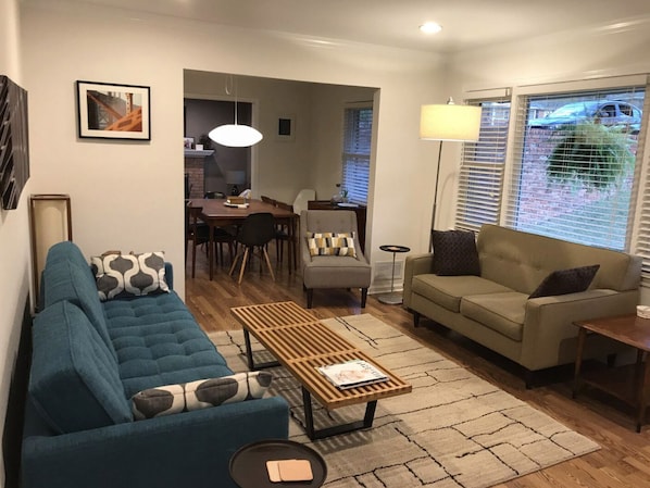 A living room with a blue sofa, a beige sofa, a wooden coffee table, and a dining area with a table and chairs.