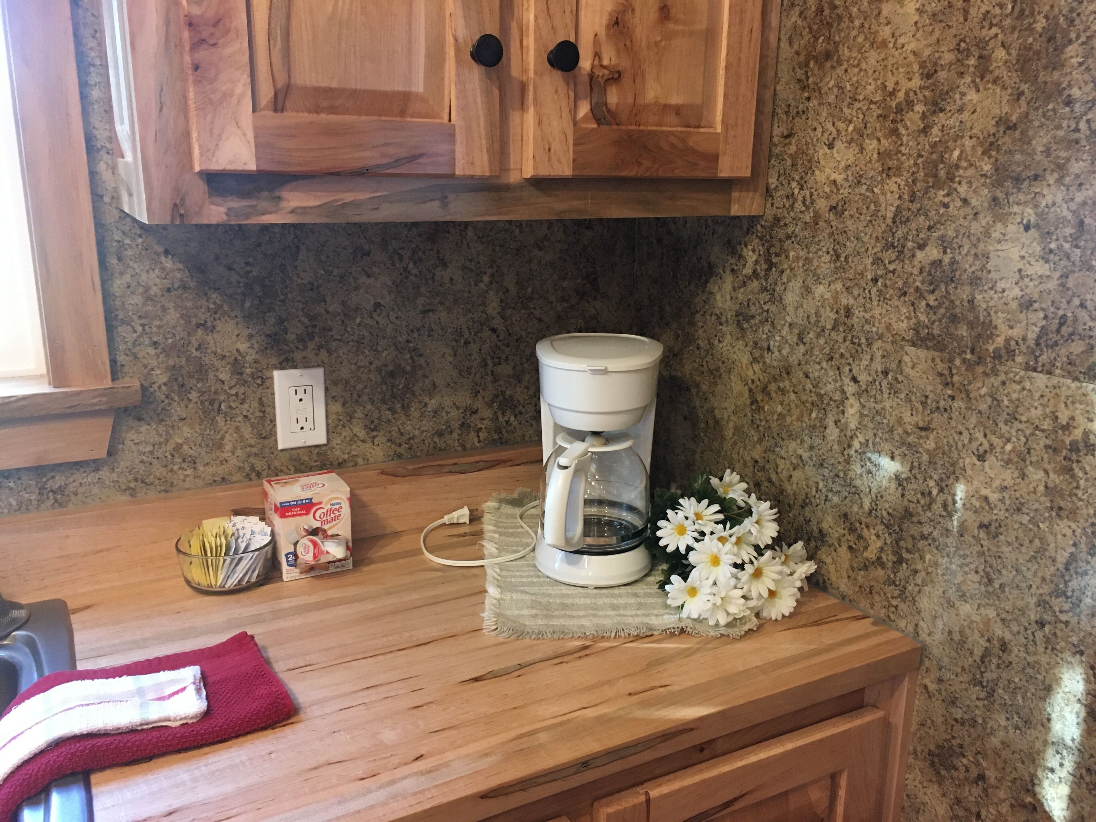 A kitchen counter with a coffee maker, a box of coffee creamer, and a red towel.