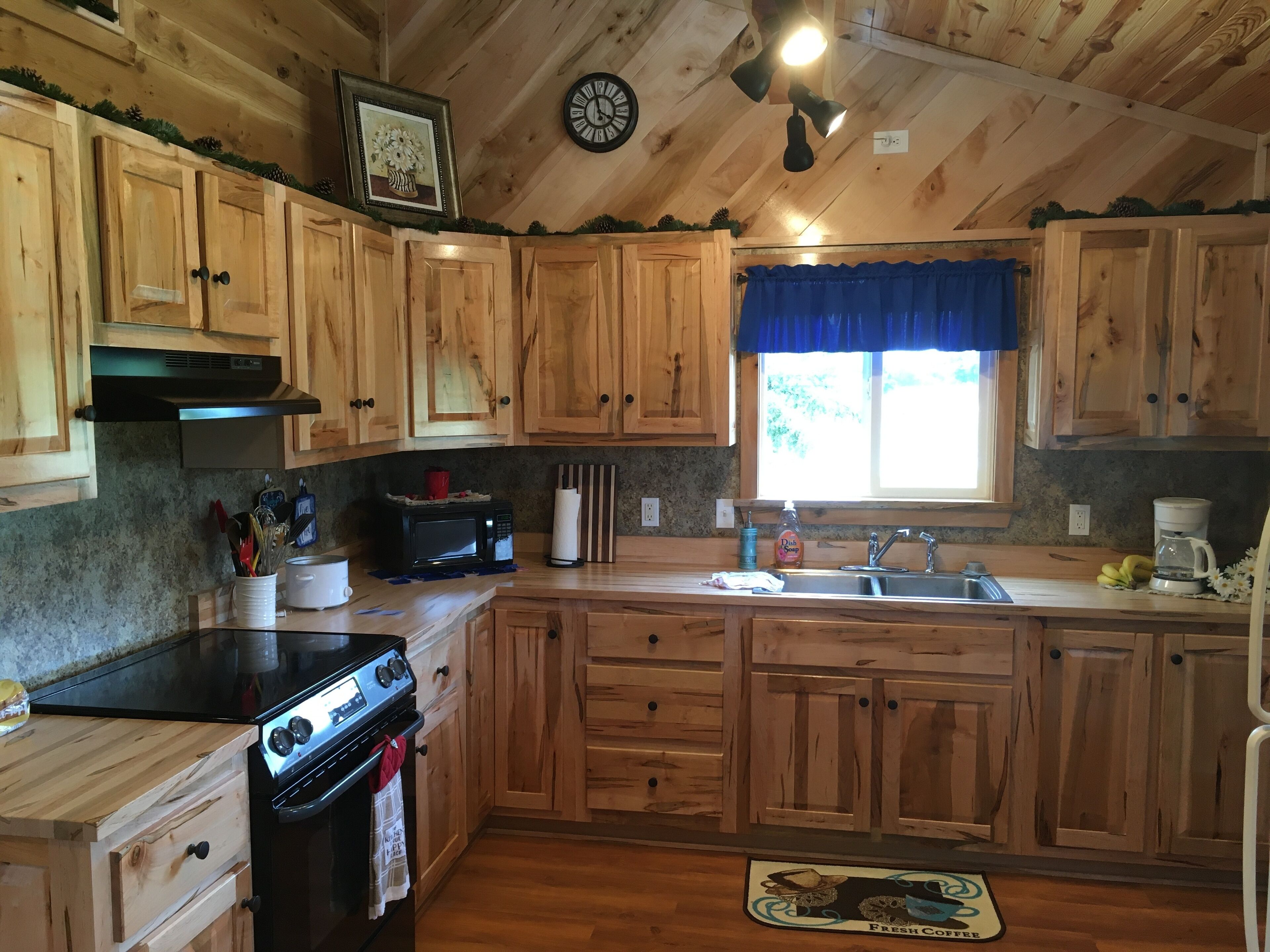 A kitchen with wooden cabinets, a stove, a sink, and a window with a blue curtain.