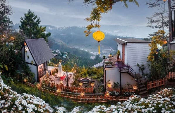 A hillside view of a house with a small garden, a wooden fence, and a lantern. - Lengkeng Da Lat Homestay (Xuan Huong - Da Lat)