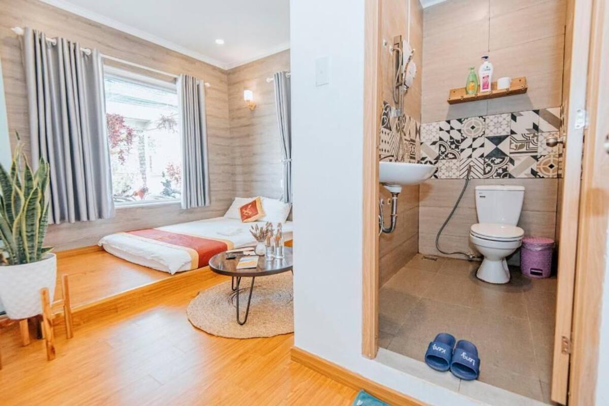 Quarto moderno com cama, mesa de cabeceira e vista para o exterior. Anexo, um banheiro com chuveiro, vaso sanitário e pia.