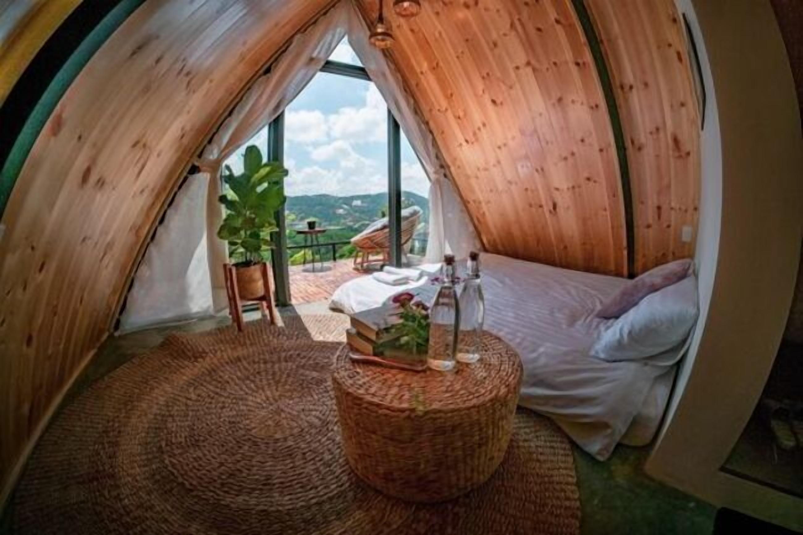 Una habitación redonda y acogedora de madera con una cama, una mesita de mimbre y vistas al exterior.