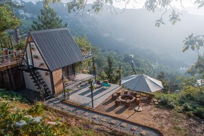 A rustic cabin with a sloped roof, a balcony, and a seating area with a table and chairs. - Lengkeng Da Lat Homestay (Xuan Huong - Da Lat)