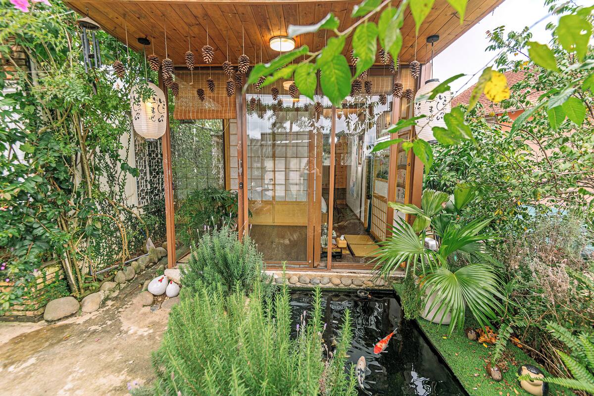 Um jardim japonês tradicional com lago de carpas, construções de madeira e vegetação exuberante.