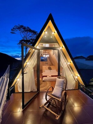 A cozy, triangular tent-style room with a bed, a TV, and a rocking chair. - Lengkeng Da Lat Homestay (Xuan Huong - Da Lat)