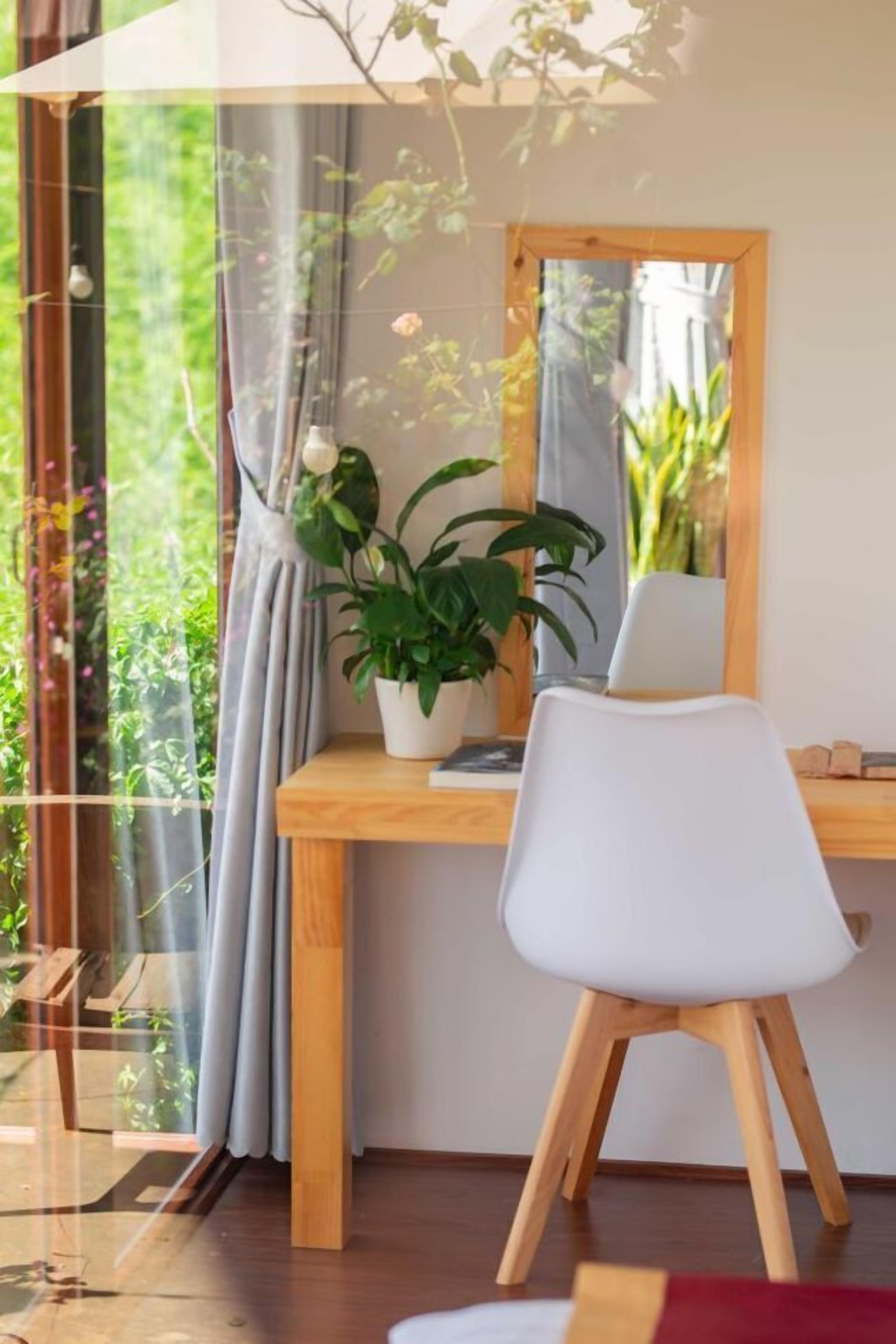A modern room with a wooden desk, a white chair, a potted plant, and a large window with curtains.
