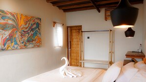 Un lit bien fait, agrémenté d’une serviette en forme de cygne, une peinture abstraite aux couleurs vives accrochée au mur et une échelle en bois appuyée contre une porte.