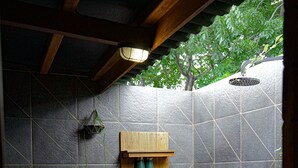 Une salle de bain avec un sol carrelé en pierre, une étagère en bois où sont posés des articles de toilette et une plante suspendue.