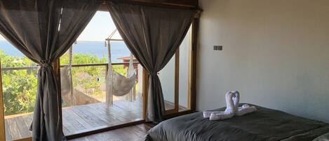 A bedroom with a bed, wooden floor, and a view of the sea through large windows.