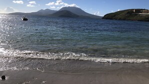 A beach with clear water, a boat, and distant mountains. - Villa Limani • Luxury Mediterranean Oasis within the Caribbean • Ocean Views (Basseterre)