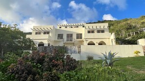A modern two-story building with a flat roof, multiple balconies, and a garden in the foreground.