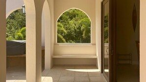 A corridor with a bench, a window with a view of greenery, and a door leading to an outdoor area.