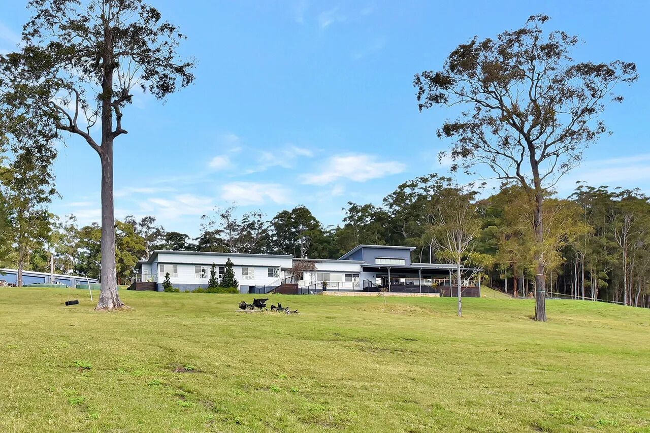 A modern two-story building with a flat roof and large windows, surrounded by a grassy field and trees.