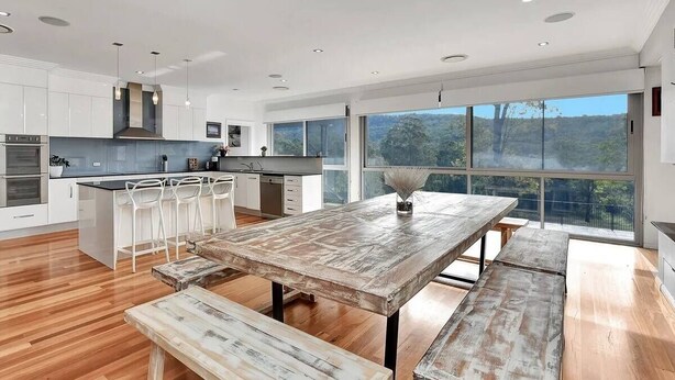 A modern kitchen with white cabinets, a wooden dining table, and a large window offering a view of the outdoors. - Luxury Mandalong Mansion with Pool & Spa (Mandalong)