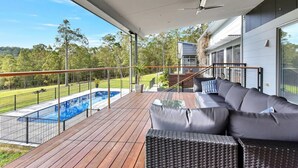 A covered outdoor deck with a pool, a sofa, and a staircase leading to a second level. - Luxury Mandalong Mansion with Pool & Spa (Mandalong)