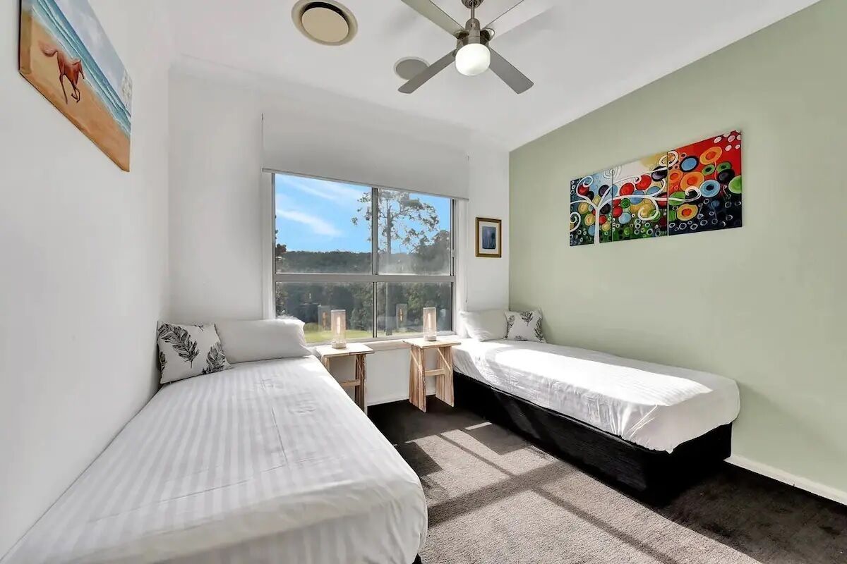 A bedroom with two beds, a desk, and a window.