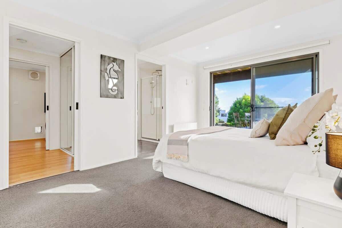A modern bedroom with a large bed, a window with a view, and a door leading to a bathroom.