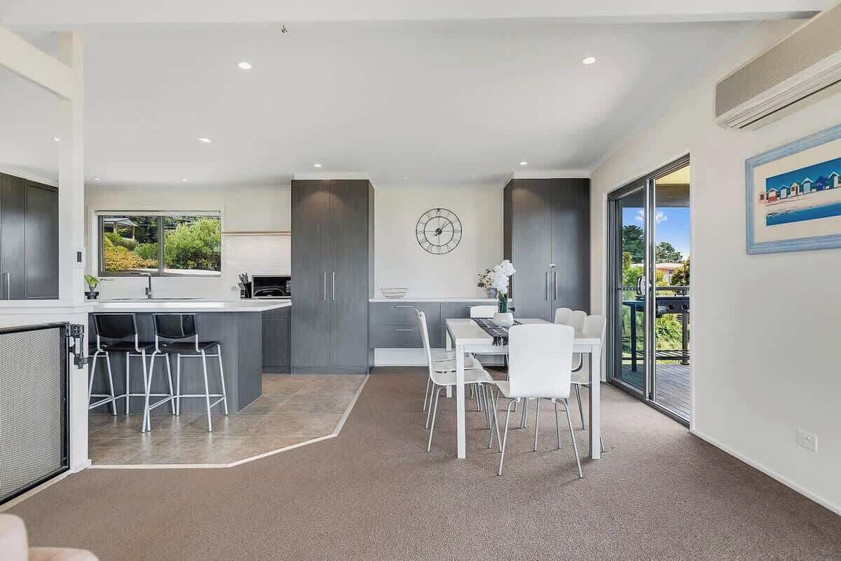 A modern kitchen with a dining area, large windows, and a view of greenery.