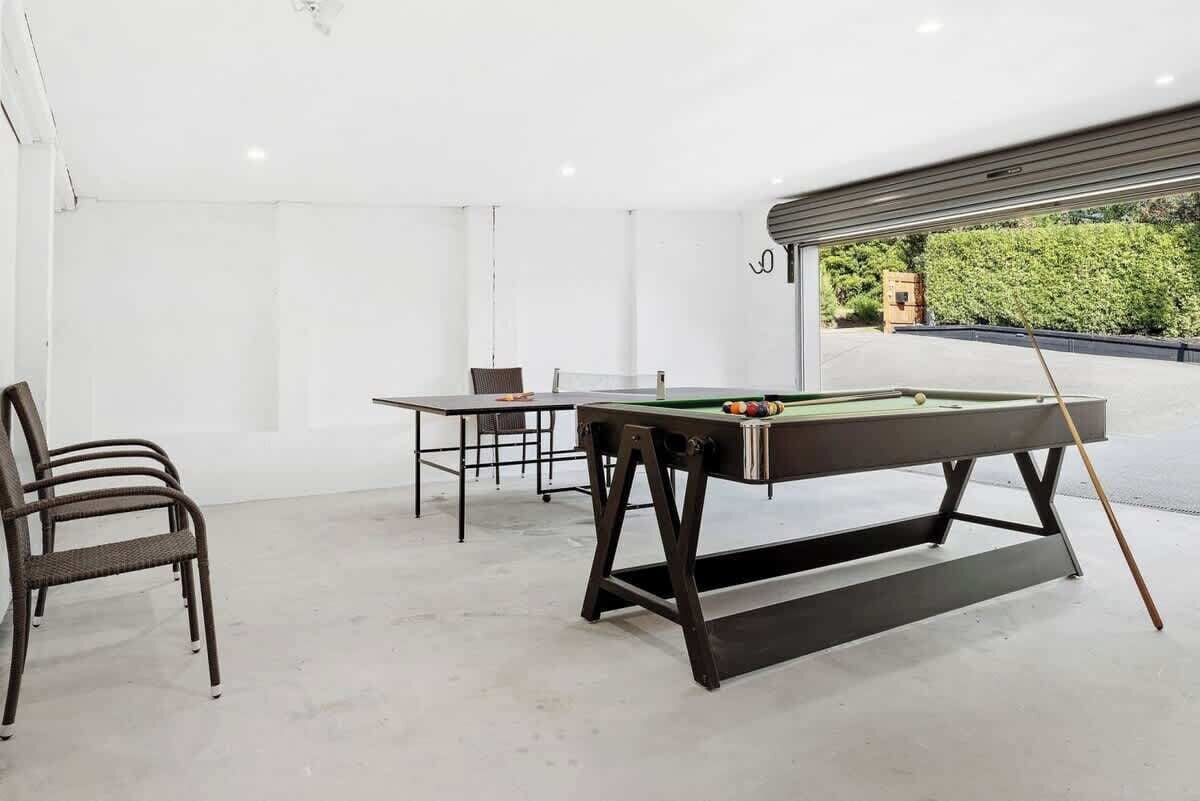 Une table de billard avec des chaises, dans une pièce spacieuse aux murs blancs et dotée d’une grande fenêtre.