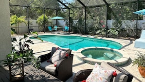 A covered outdoor area with a swimming pool, two wicker chairs with cushions, and potted plants.