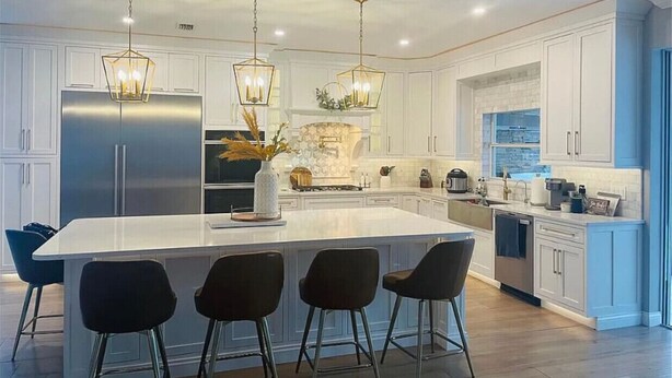 A modern kitchen with white cabinetry, a central island with bar stools, stainless steel appliances, and pendant lighting.