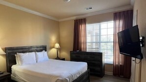 Habitación de hotel con cama, mesita de noche, cómoda, televisor y ventana con cortinas.